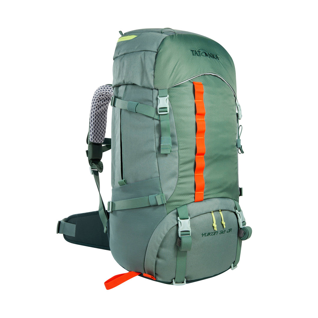 Front three quarter view of 32 litre Tatonka branded Yukon 32 JR pack with load control straps, side compression straps, compression around perimeter of base, zipped side pockets with expansion pleats and standard side pockets. Also features Gear loops on lid, front daisy chain, and hiking pole fixation points – Sage Green with Orange highlights