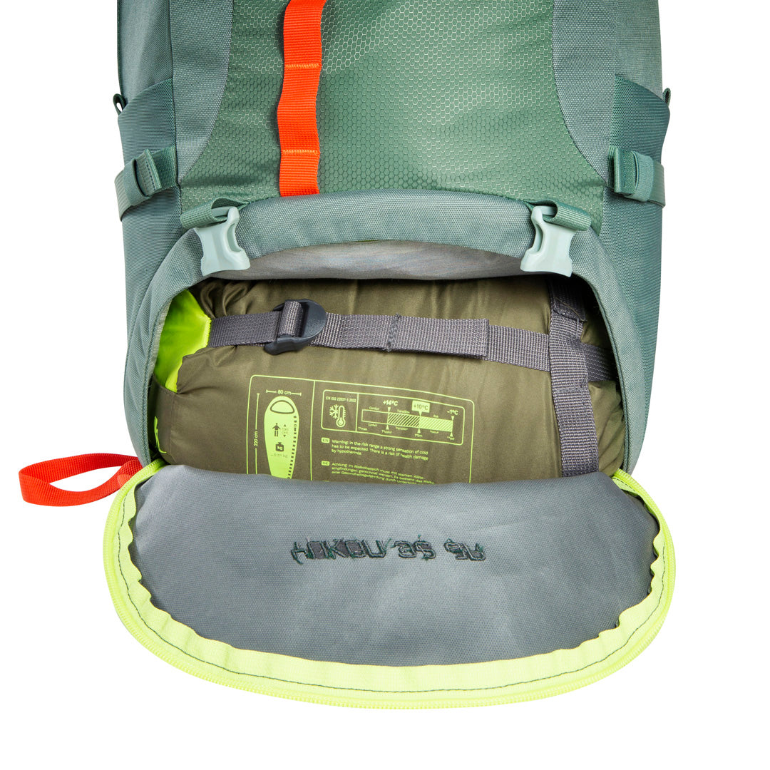 Front view of 32 litre Tatonka branded Yukon 32 JR pack showing bottom compartment unzipped fully with compression straps showing – Sage Green with Orange and pale yellow highlights