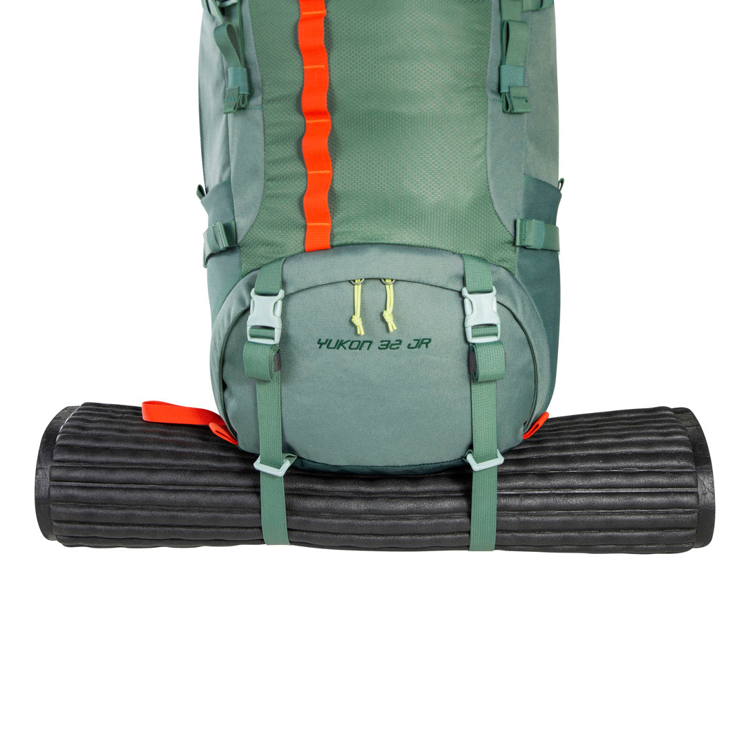 Close up of black bed roll (not included) held in place beneath base of 32 litre Tatonka branded Yukon 32 JR pack using load control straps – Sage Green